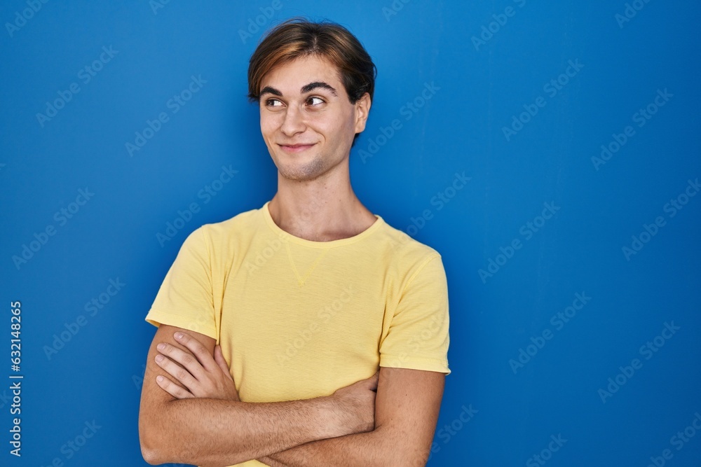 Young man standing over blue background smiling looking to the side and staring away thinking. Young man standing over blue background smiling looking to the side and staring away thinking.