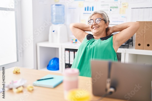 Middle age grey-haired woman business worker relaxed with hands on head at office