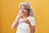 Middle age woman with grey hair standing over yellow background pointing fingers to camera with happy and funny face. good energy and vibes.