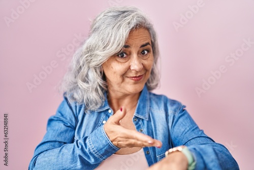Middle age woman with grey hair standing over pink background in hurry pointing to watch time, impatience, upset and angry for deadline delay