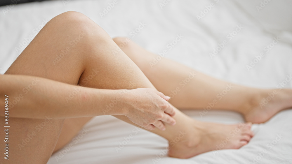Young blonde woman sitting on bed massaging leg at bedroom