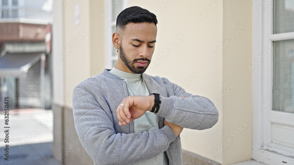 Young hispanic man with serious face looking watch at street Young hispanic man with serious face looking watch at street