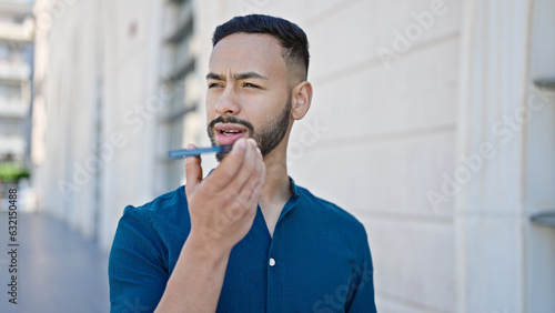 Young hispanic man sending voice message with smartphone at street