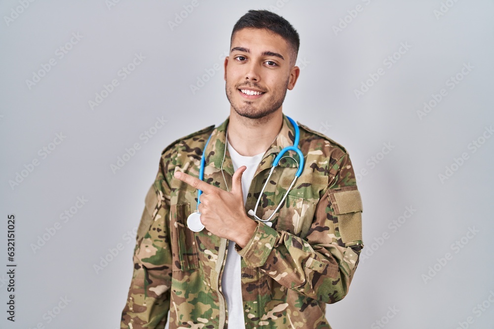Young hispanic doctor wearing camouflage army uniform smiling cheerful pointing with hand and finger up to the side Young hispanic doctor wearing camouflage army uniform smiling cheerful pointing with hand and finger up to the side
