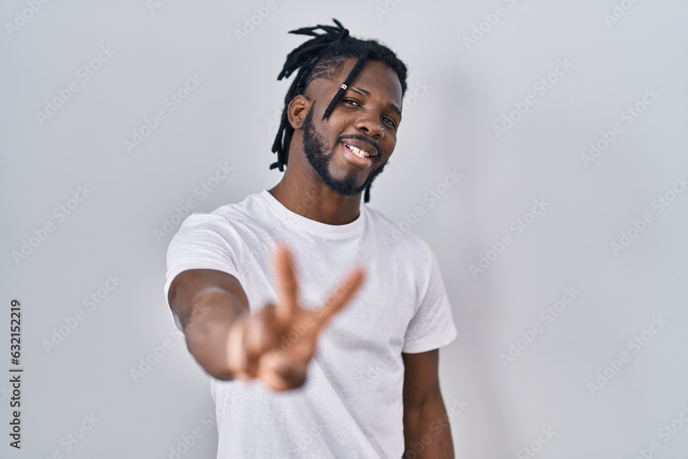 African man with dreadlocks wearing casual t shirt over white background smiling looking to the camera showing fingers doing victory sign. number two. African man with dreadlocks wearing casual t shirt over white background smiling looking to the camera showing fingers doing victory sign. number two.