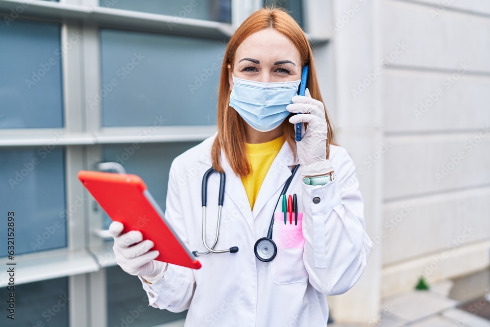 Young caucasian woman doctor wearing medical mask using touchpad talking on smartphone at hospital Young caucasian woman doctor wearing medical mask using touchpad talking on smartphone at hospital