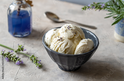 Lavender ice cream in a grey bowl with lavender syrup in a a bottle, fresh lavender branches and tea spoon on grey concrete background