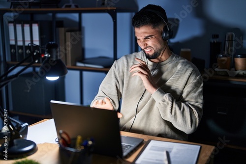 Fotografie Young handsome man working using computer laptop at night disgusted expression, displeased and fearful doing disgust face because aversion reaction