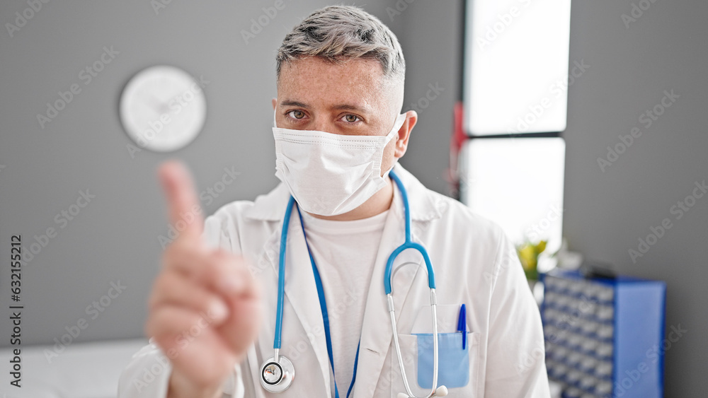 Young caucasian man doctor wearing medical mask saying no with finger at the clinic Young caucasian man doctor wearing medical mask saying no with finger at the clinic