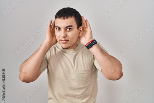 Young arab man wearing casual t shirt trying to hear both hands on ear gesture, curious for gossip. hearing problem, deaf