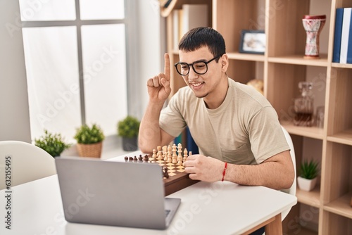 Young arab man playing chess online smiling with an idea or question pointing finger with happy face, number one