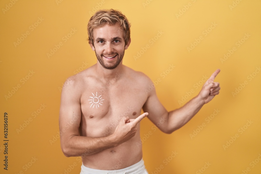 Caucasian man standing shirtless wearing sun screen smiling and looking at the camera pointing with two hands and fingers to the side.