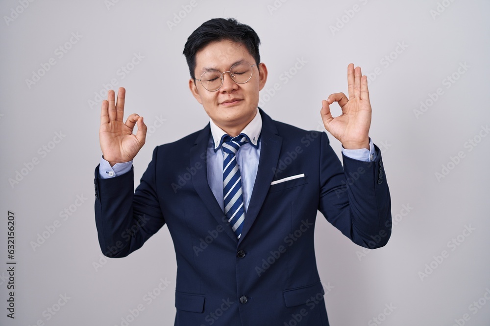 Young asian man wearing business suit and tie relaxed and smiling with eyes closed doing meditation gesture with fingers. yoga concept. Young asian man wearing business suit and tie relaxed and smiling with eyes closed doing meditation gesture with fingers. yoga concept.