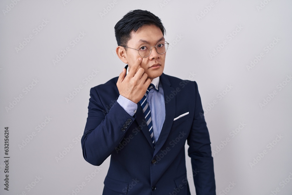 Young asian man wearing business suit and tie pointing to the eye watching you gesture, suspicious expression Young asian man wearing business suit and tie pointing to the eye watching you gesture, suspicious expression