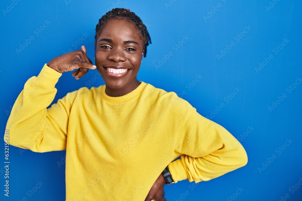 Beautiful black woman standing over blue background smiling doing phone gesture with hand and fingers like talking on the telephone. communicating concepts. Beautiful black woman standing over blue background smiling doing phone gesture with hand and fingers like talking on the telephone. communicating concepts.