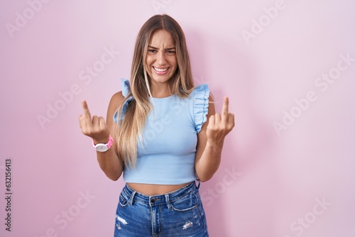Fotografie Young blonde woman standing over pink background showing middle finger doing fuck you bad expression, provocation and rude attitude
