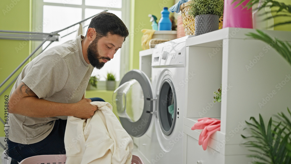 Obraz premium Young hispanic man washing clothes at laundry room