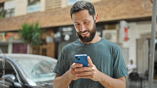 Young hispanic man using smartphone and earphones smiling at street
