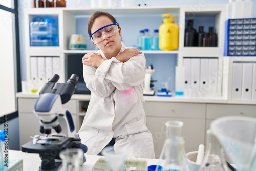 Hispanic girl with down syndrome working at scientist laboratory hugging oneself happy and positive  smiling confident. self love and self care