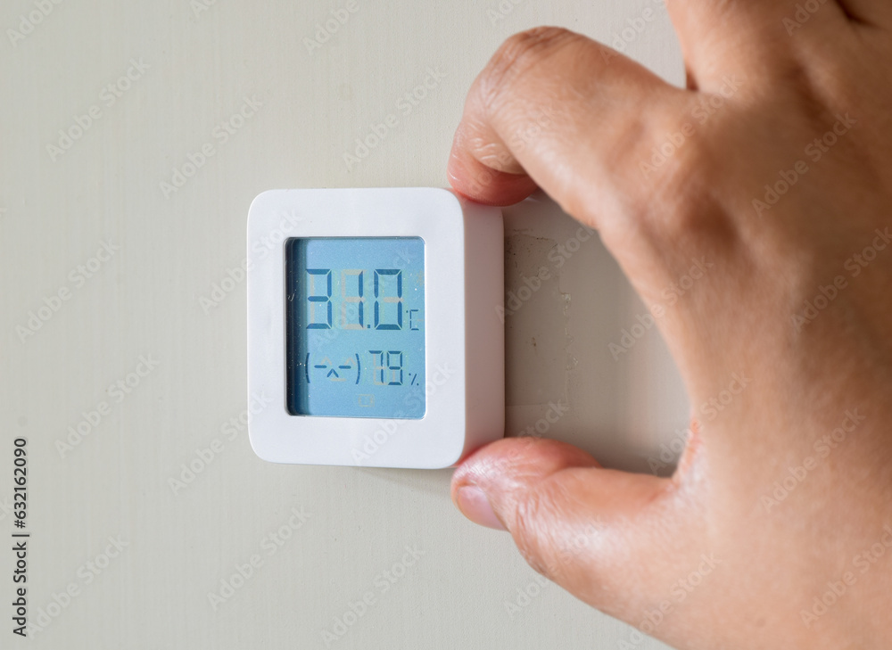 Hand holding home hygrometer and temperature indicator electronic device and fixing it on wall. Uncomfortable indoor climate. Hand holding home hygrometer and temperature indicator electronic device and fixing it on wall. Uncomfortable indoor climate.