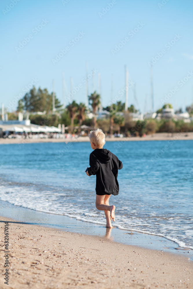 Child playing on ocean beach. Kid jumping in the waves at sunset. Sea vacation for family with kids. Little boy running on tropical beach of exotic island during summer holiday. Swim wear for children Child playing on ocean beach. Kid jumping in the waves at sunset. Sea vacation for family with kids. Little boy running on tropical beach of exotic island during summer holiday. Swim wear for children