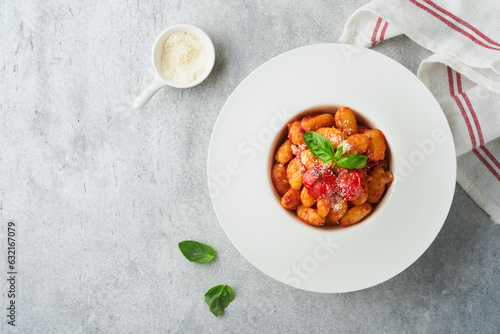 Potato gnocchi. Traditional homemade potato gnocchi with tomato sauce, basil and parmesan cheese on kitchen table on light grey kitchen table background. Traditional Italian food. Top view.