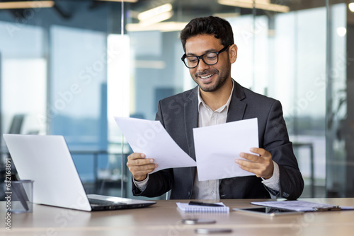 Successful mature experienced financier on paper work, Arab smiling satisfied with results of financial achievement, reviewing contracts, invoices and statements with accounts, businessman in suit.