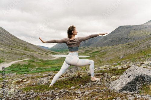 A slender woman is a trainer performing the exercise in the mountains in the nature of the north. Training in comfortable modern sportswear. Beautiful figure and flexible body.