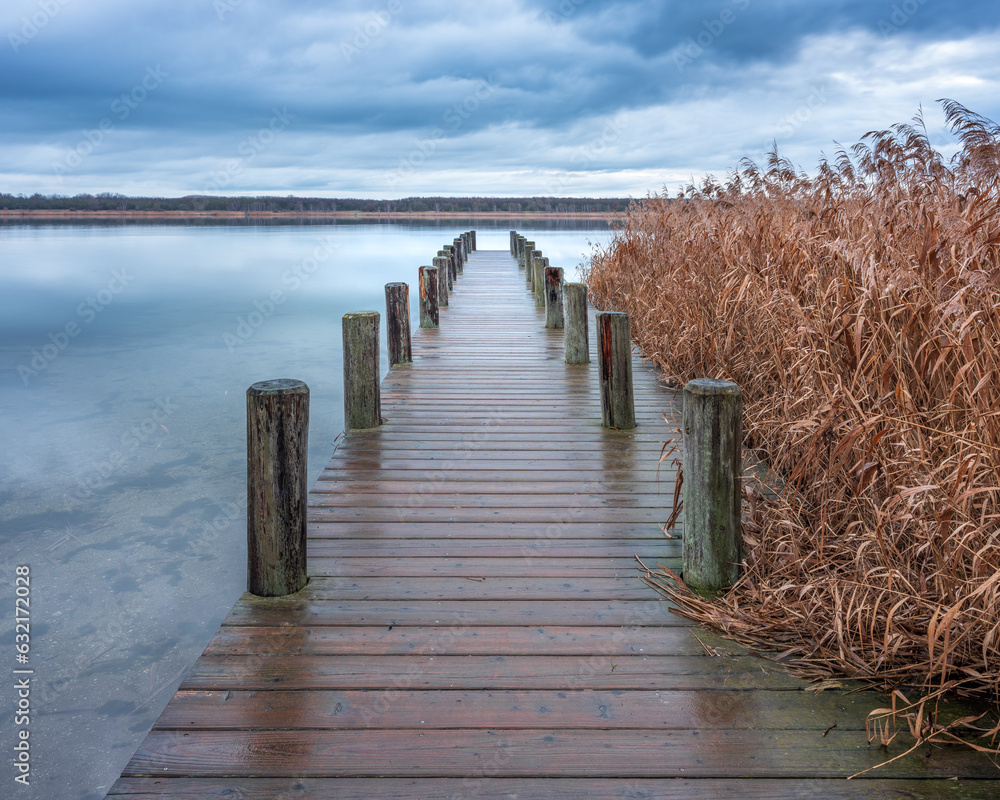 Calm Lake with Wooden Pier and Reeds under stormy overcast sky in winter