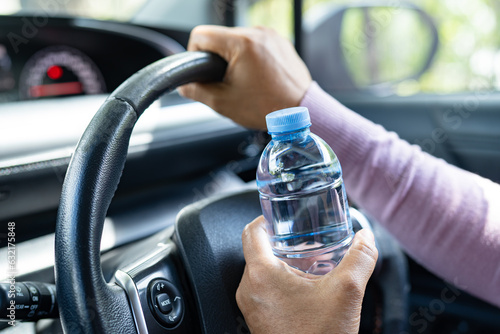 Asian woman driver holding bottle for drink water while driving a car. Plastic hot water bottle cause fire.