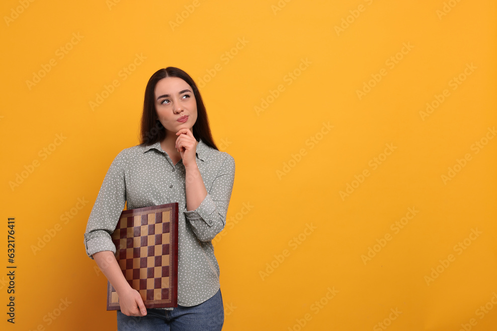 Thoughtful woman with chessboard on orange background, space for text Thoughtful woman with chessboard on orange background, space for text