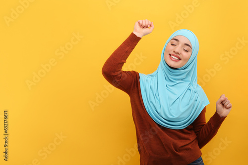 Muslim woman in hijab dancing on orange background, space for text © New Africa