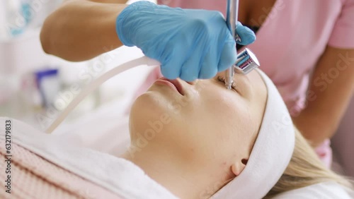 Beautician cosmetologist makes a procedure for skin face non-injection oxygen mesotherapy with air pressure with device. Hardware cosmetology in clinic salon for client.	 photo