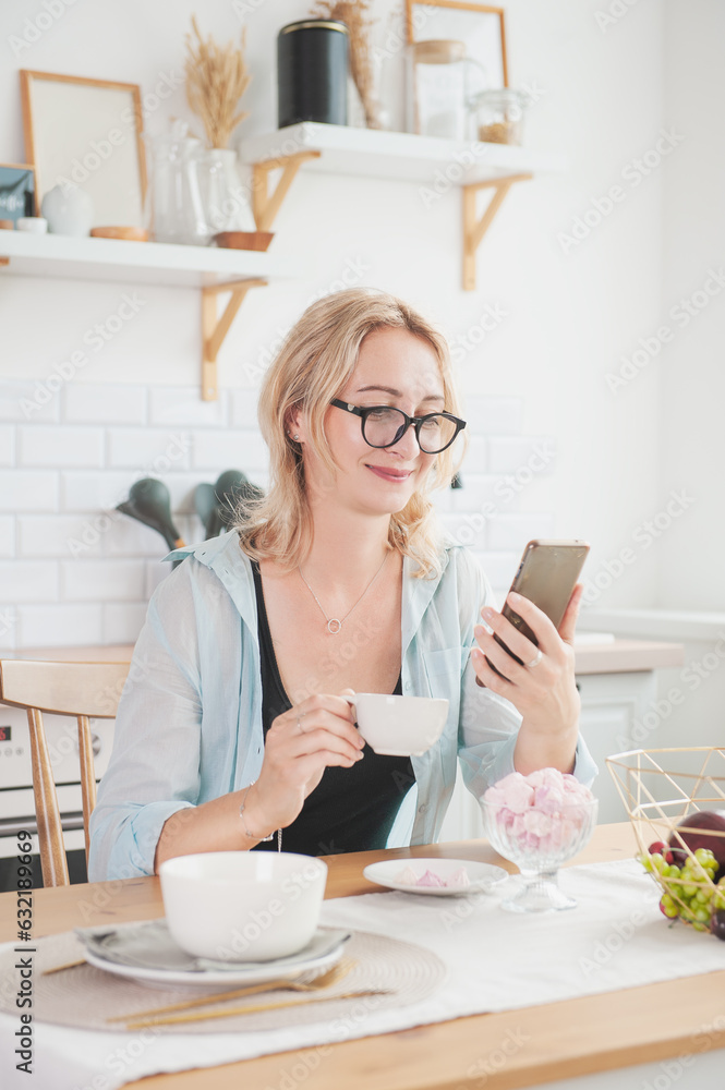 Smiling beautiful woman with cup of coffee and mobile phone in the kitchen