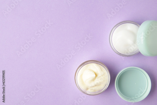 Facial cosmetic cream in transparent open jar, beauty product on purple background. Space for text