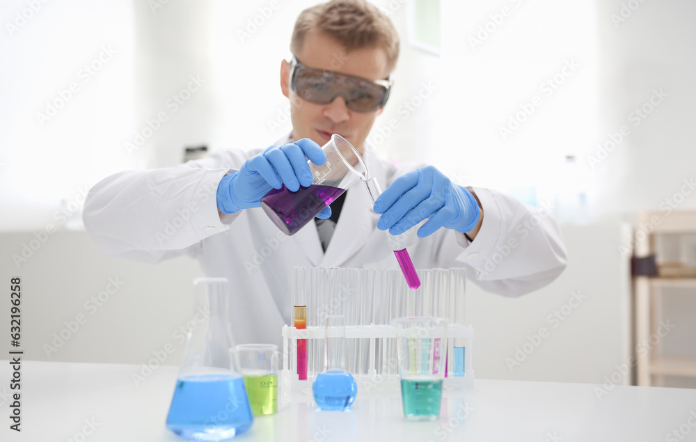 Male chemist holds test tube of glass in his hand overflows liquid solution of potassium permanganate. Conducts an analysis reaction takes various versions of reagents using chemical manufacturing Male chemist holds test tube of glass in his hand overflows liquid solution of potassium permanganate. Conducts an analysis reaction takes various versions of reagents using chemical manufacturing