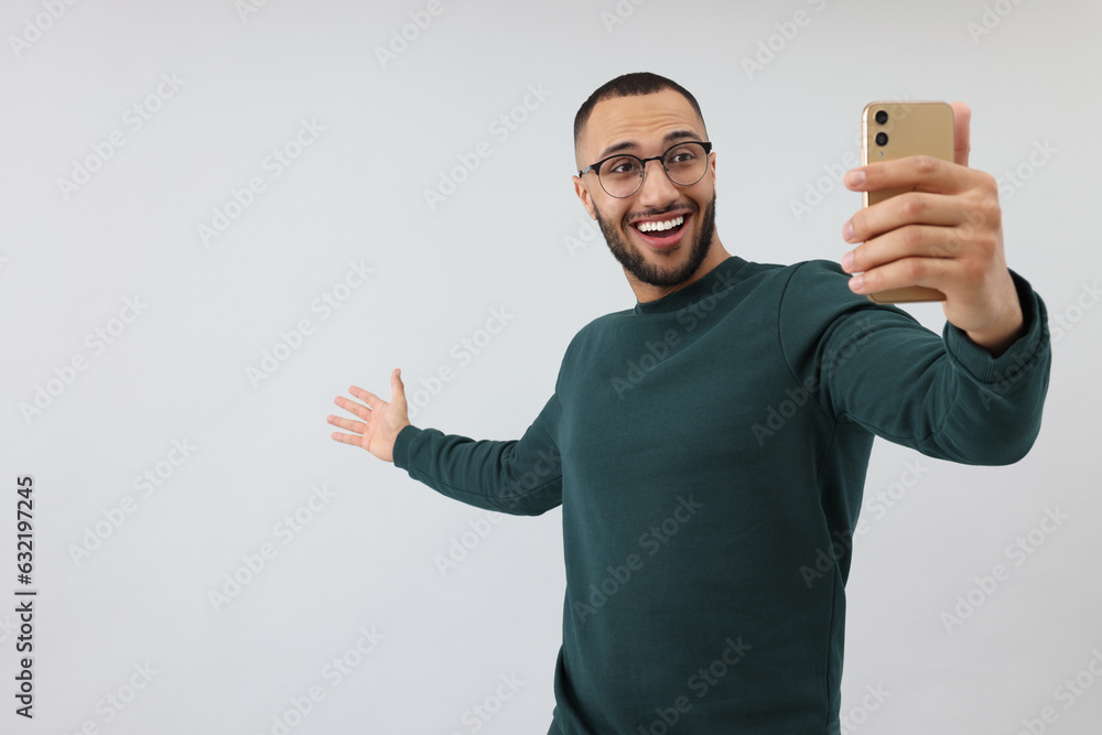 Smiling young man taking selfie with smartphone on grey background, space for text Smiling young man taking selfie with smartphone on grey background, space for text