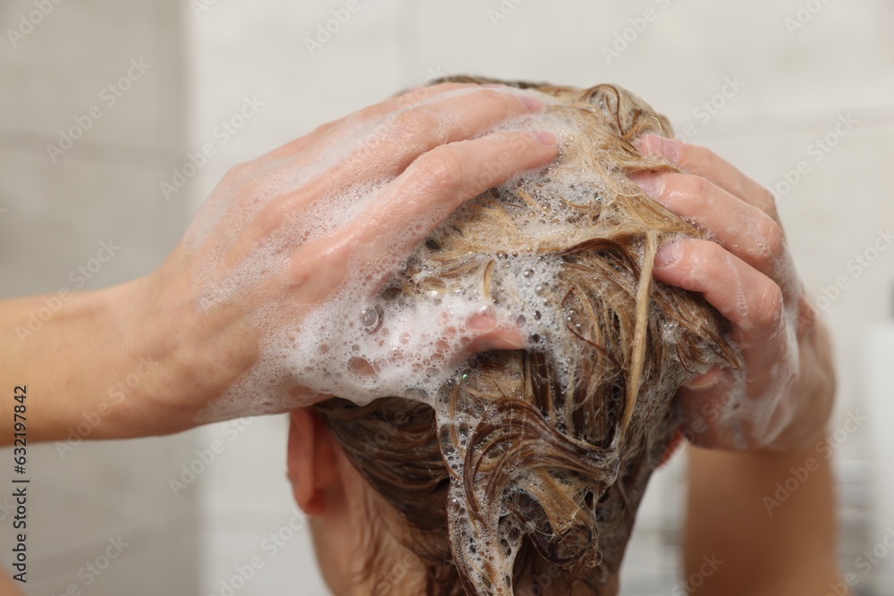 Woman washing hair with shampoo indoors, closeup