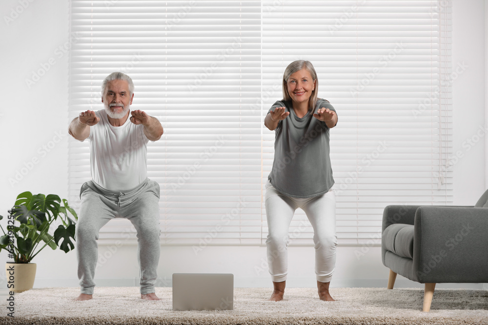 Obraz premium Senior couple practicing yoga with laptop on carpet at home