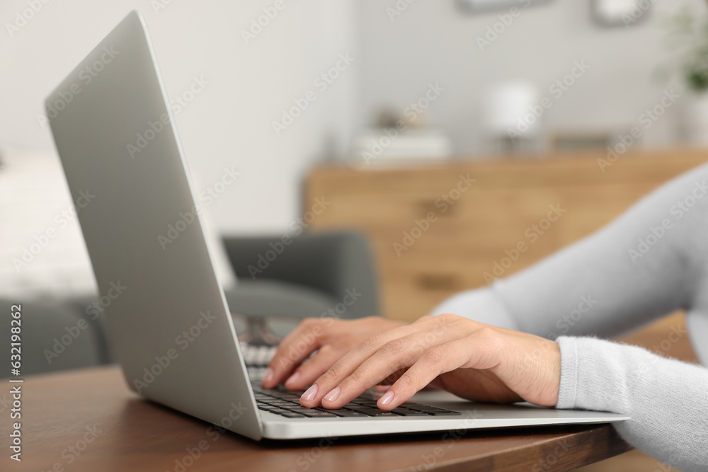 Fototapeta premium Woman using laptop at wooden coffee table in room, closeup