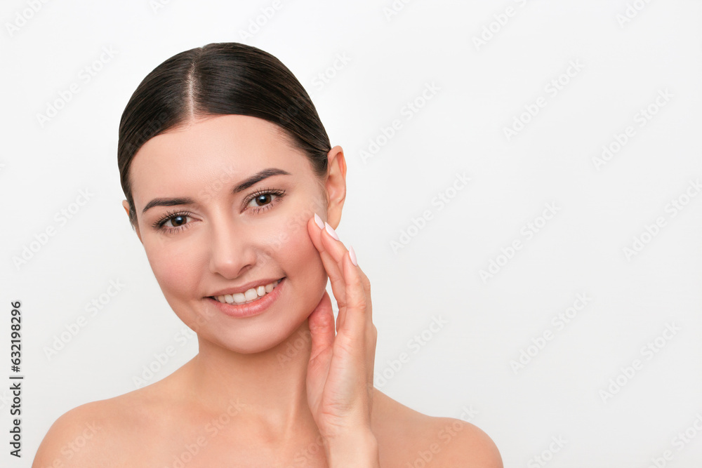 A portrait of young attractive happy beautiful Caucasian dark-haired woman touching her face with her hand and enjoying clean and beautiful skin. Isolated on a light background.  Skin care concept