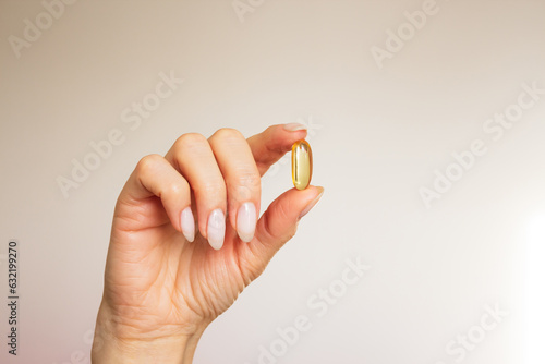 Fotografía woman's hand holdind with her fingers a soft yellow gel capsule close-up on a beige background with sunlight