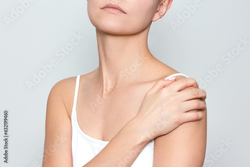 a young woman in white underwear holds her shoulder with her hand, suffers from severe shoulder pain, isolated on a light background