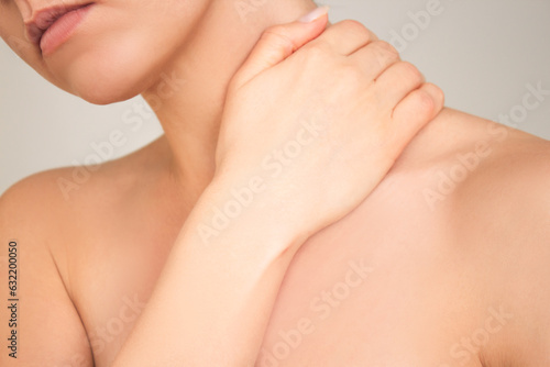 a close-up shot of a young naked woman who suffering from osteochondrosis, experiencing neck pain, holding her hand to her neck. photo