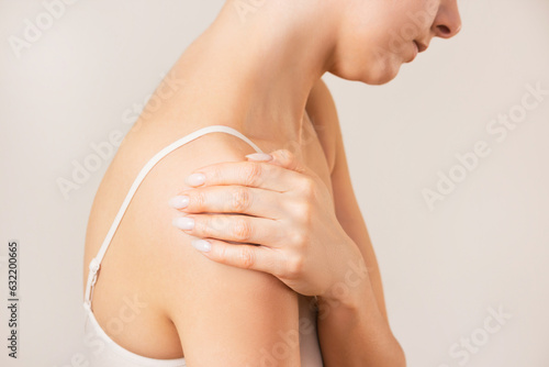 profile of a young woman in white underwear, suffering from bursitis, experiencing acute pain in the shoulder joint. Shoulder injury. Isolated on a beige background.