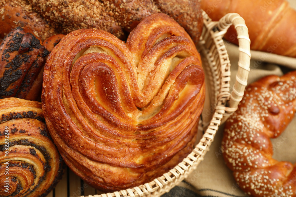 Fototapeta premium Wicker basket with different tasty freshly baked pastries on table, closeup