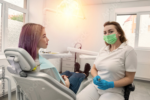 patient sitting dental chair next to female dentist doctor who is conducting an examination.