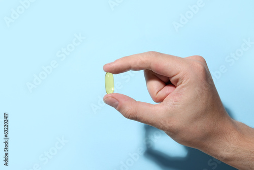 Man holding pill on light blue background, closeup