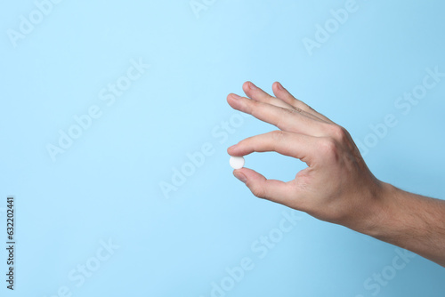 Man holding pill on light blue background, closeup. Space for text