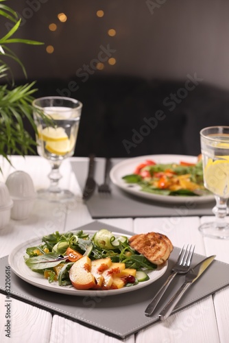 Delicious salad with peach slices served on white wooden table
